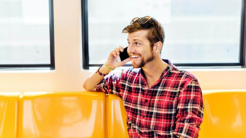 A smiling person sitting on a train talking on a smartphone.