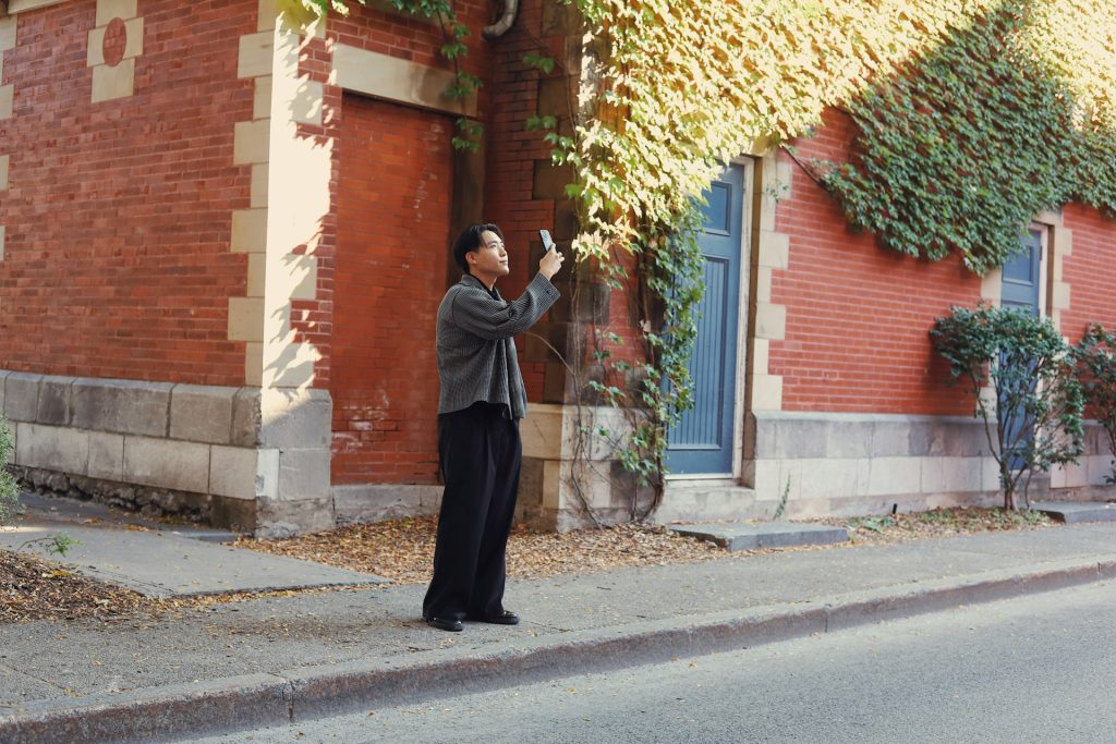 A man standing on the side of the road, taking a photo of the building across him.