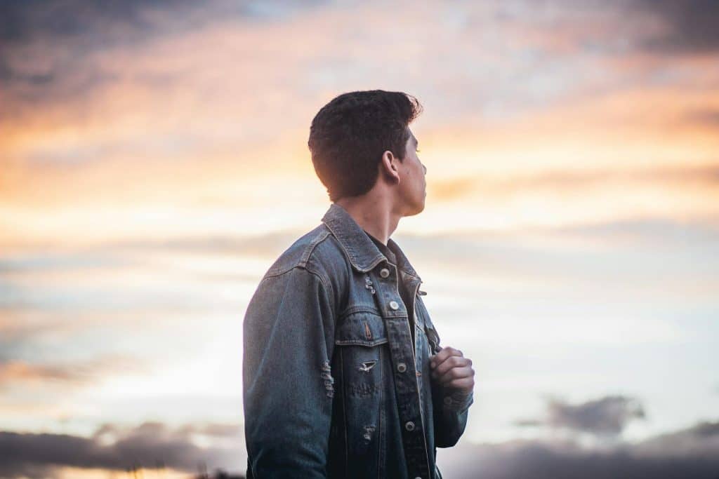A man wearing a denim jacket looking at the sky.