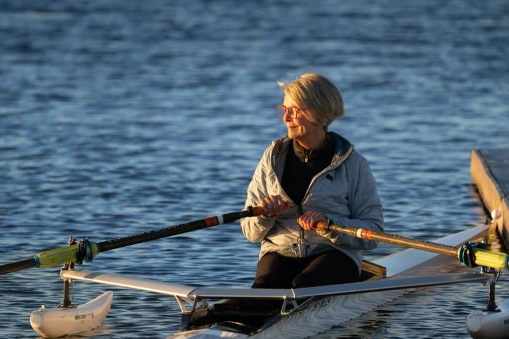A woman rowing her boat on calm water.