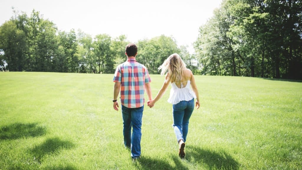 A man and woman walking on a green grass field surrounded with trees.