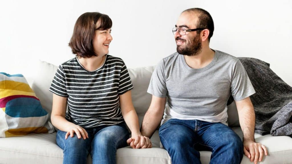 Smiling woman in glasses and striped shirt holding hands with a smiling man.