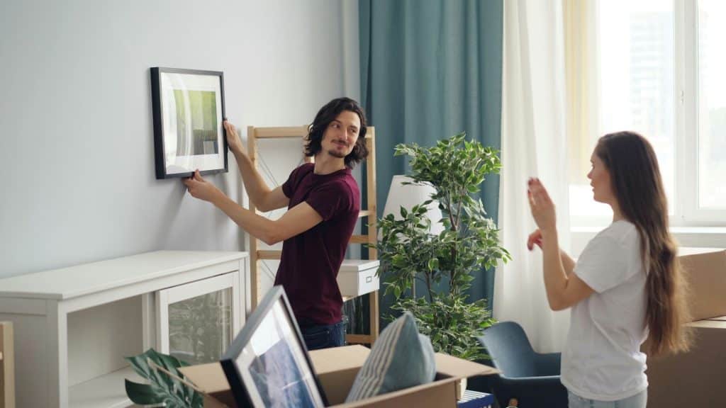 A woman giving instructions to the man where to put the picture frame.