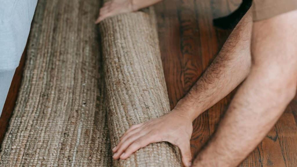 A person rolling up a woven rug on a wooden floor.