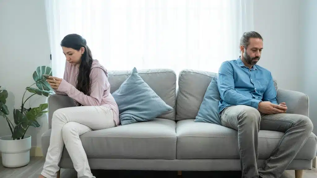 A couple sitting on opposite sides of a couch and using their phones.