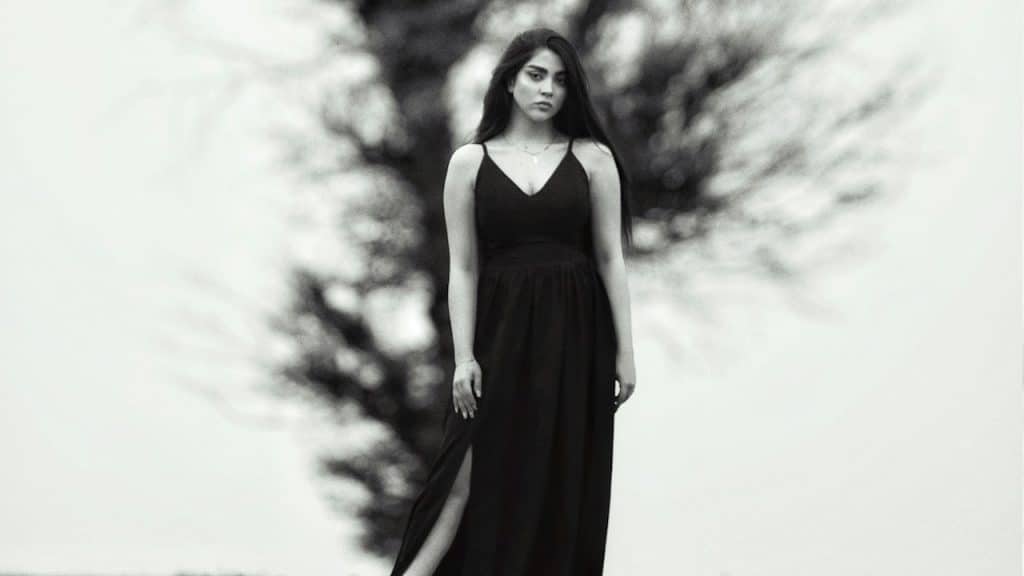 A woman in a long black dress standing in front of a tree.