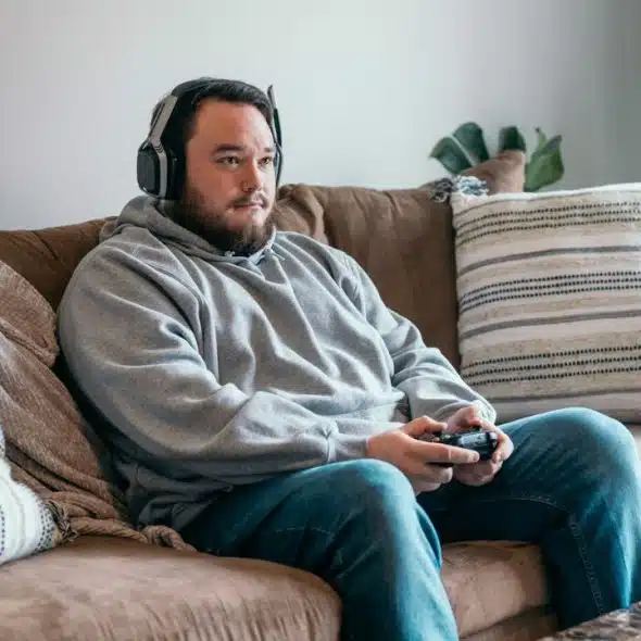 Man wearing headphones and holding a controller, sitting on a brown couch.