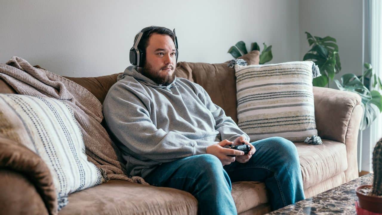 Man wearing headphones and holding a controller, sitting on a brown couch.