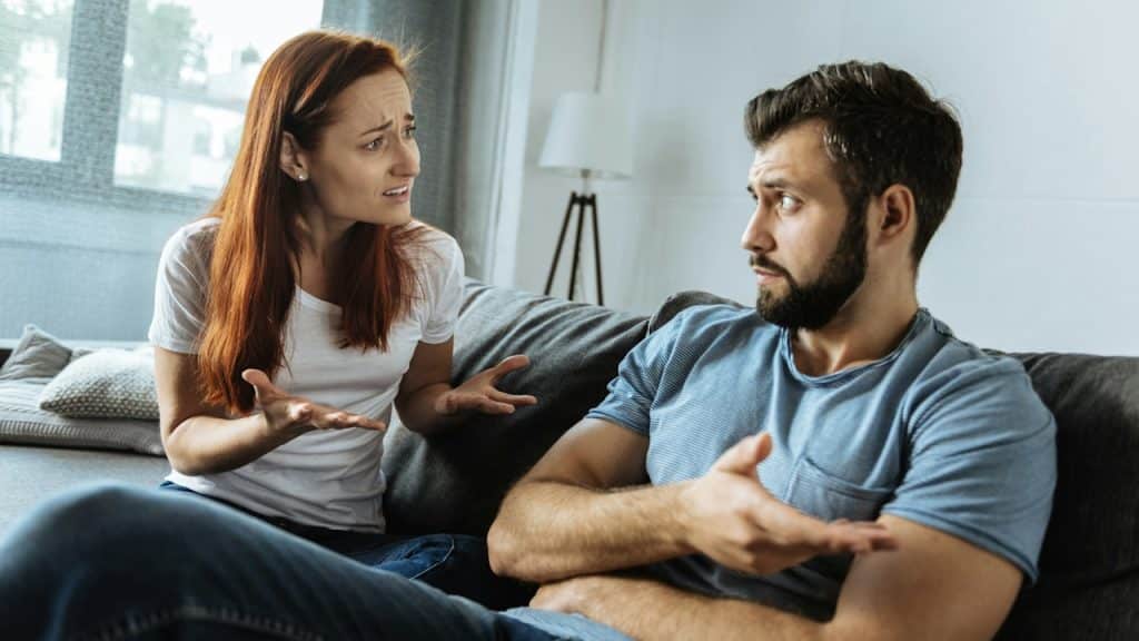 A woman complaining to her husband, who is sitting next to her on a couch.