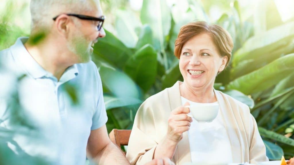 Smiling woman holding a white cup talking to a man with glasses outdoors.