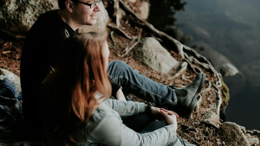 A couple sitting on a rock near a body of water.