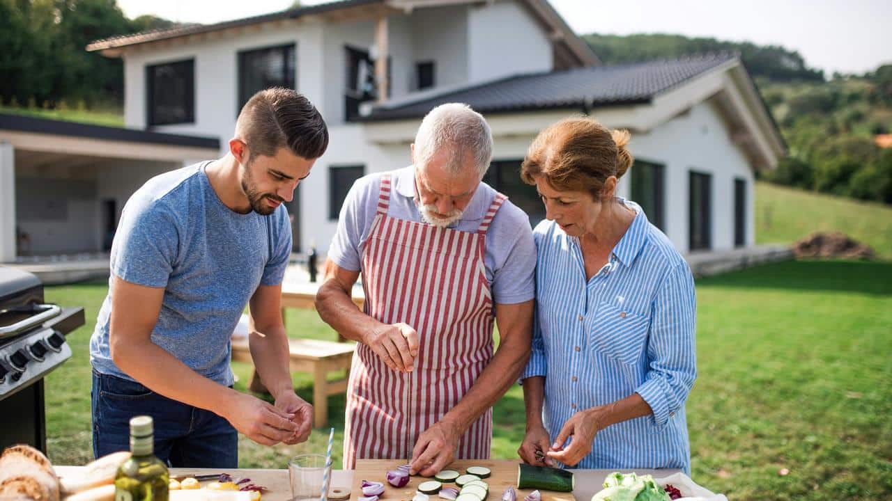 A family of three chopping vegetables outdoors at a table.