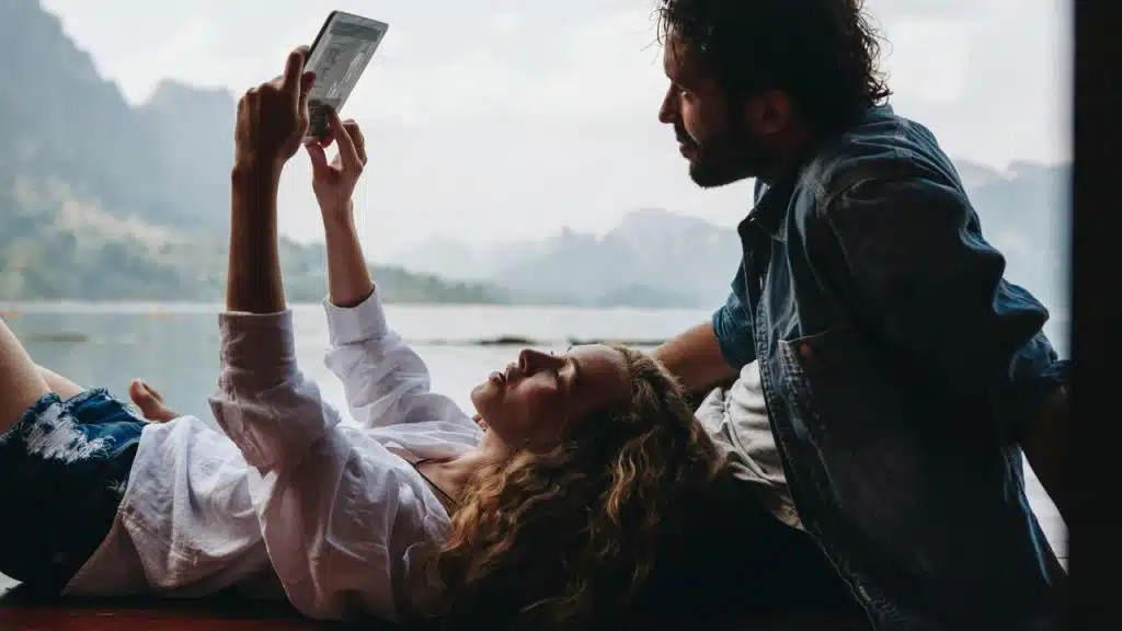 A couple relaxing by the water with one person holding a tablet.