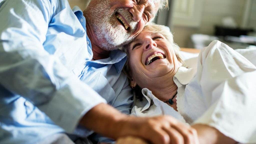 An older couple lying down together and laughing joyfully.