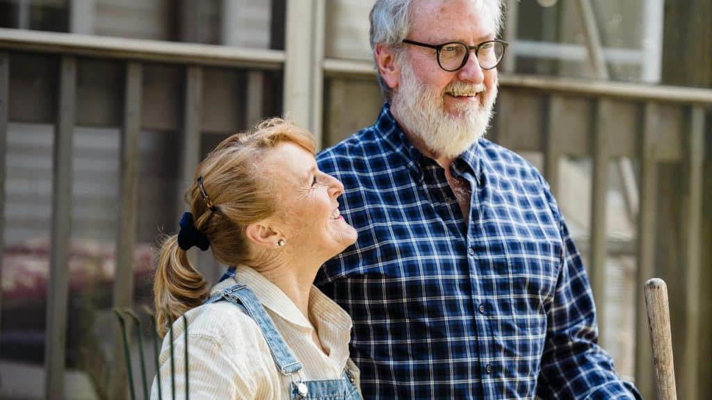 A senior couple standing outdoors, smiling at each other.