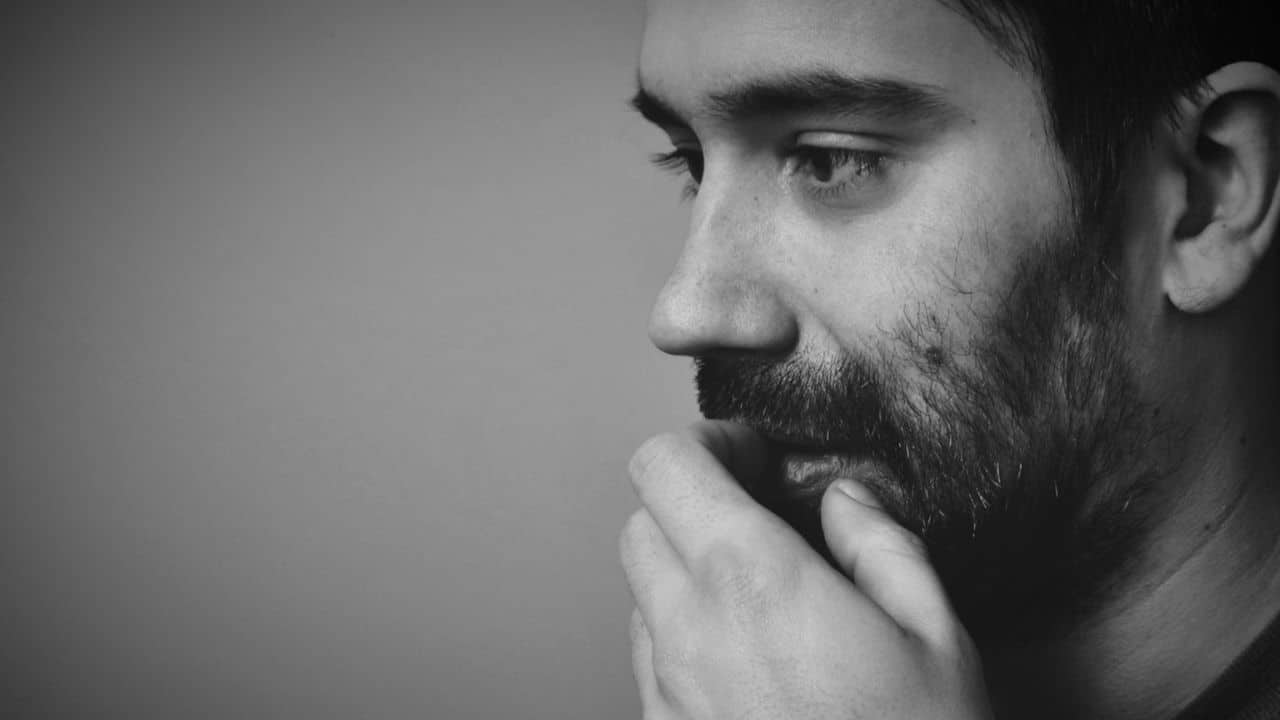 Black and white close-up of a man's pensive profile, hand resting on his mouth.