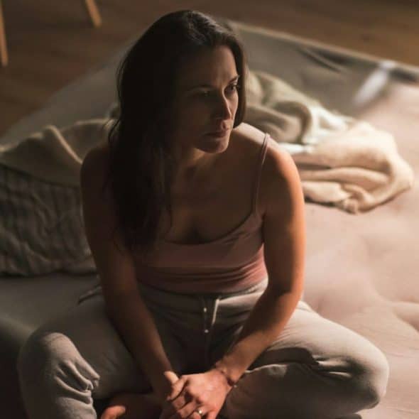 Woman sitting alone and looking distressed on a bed in a dimly lit room.