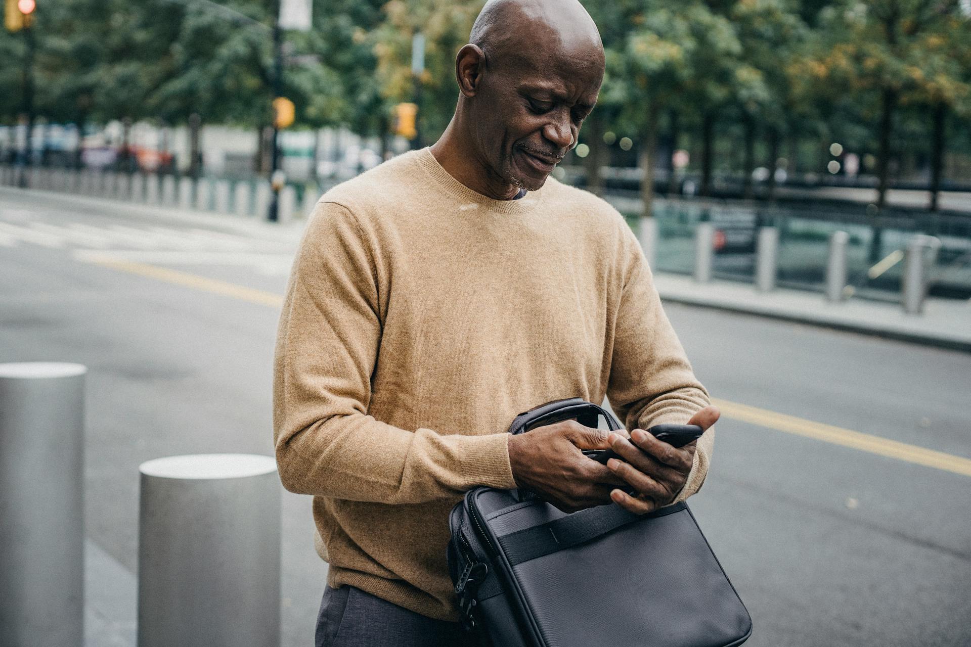 A man browsing his smartphone at the side of the street.