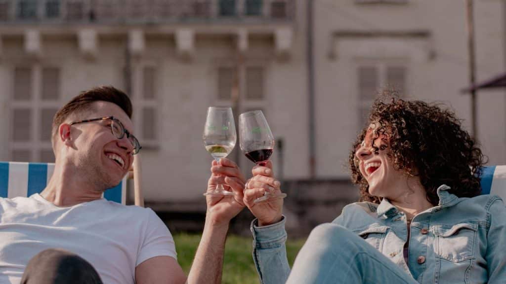 A smiling pair clinking wine glasses while relaxing outdoors.