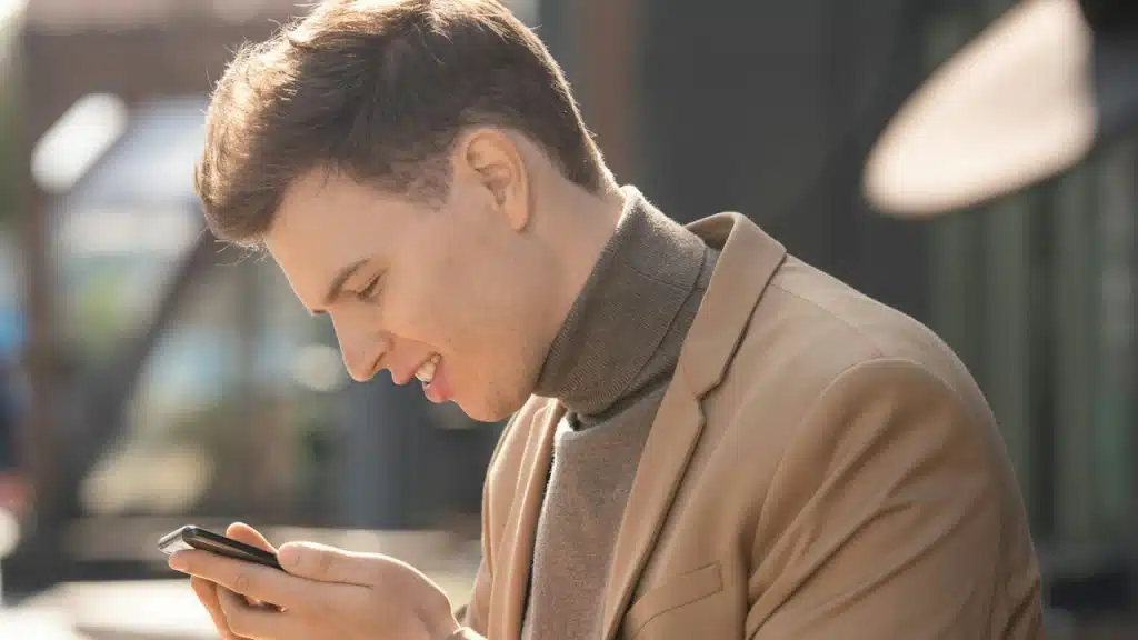 A man smiling while he uses his phone.
