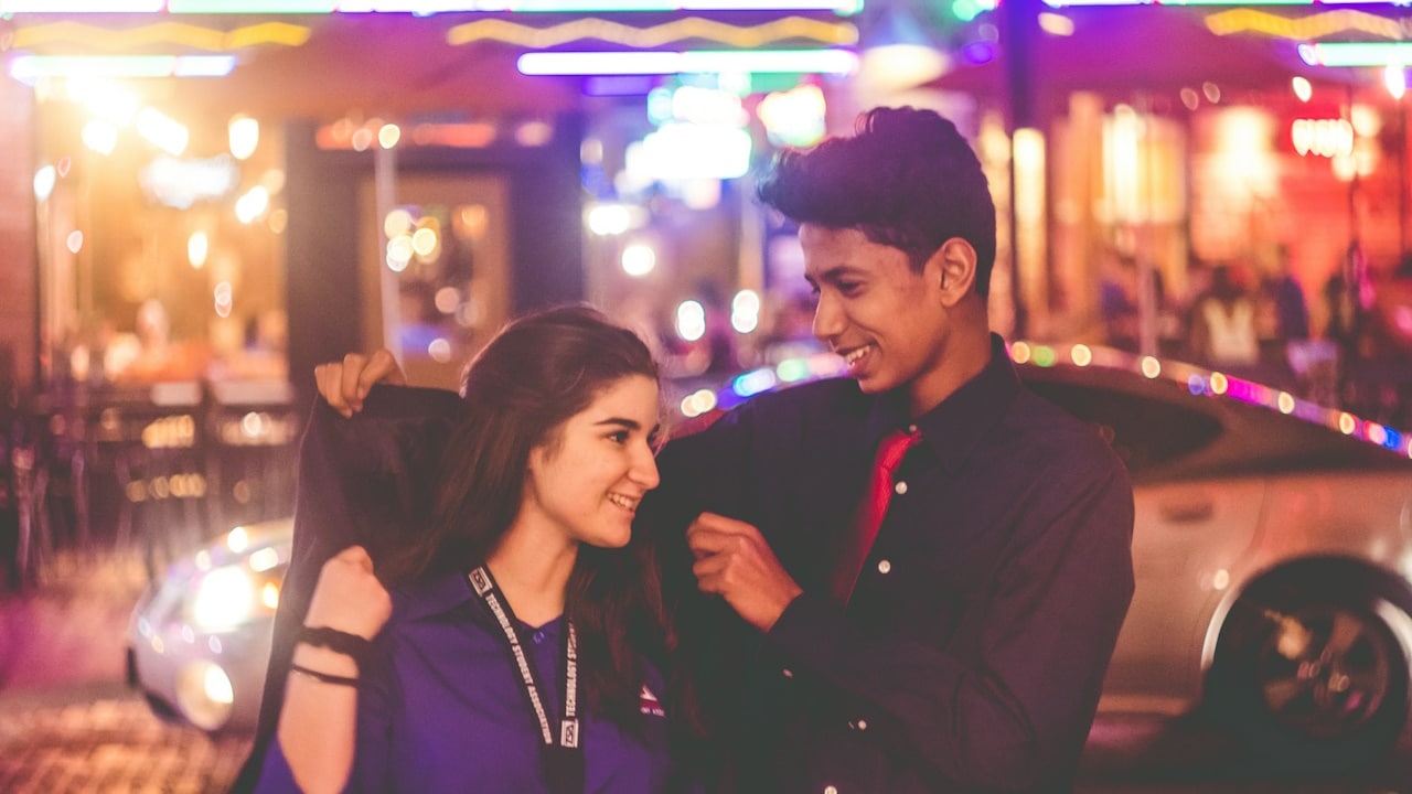 A young man giving his coat to his girlfriend to wear.