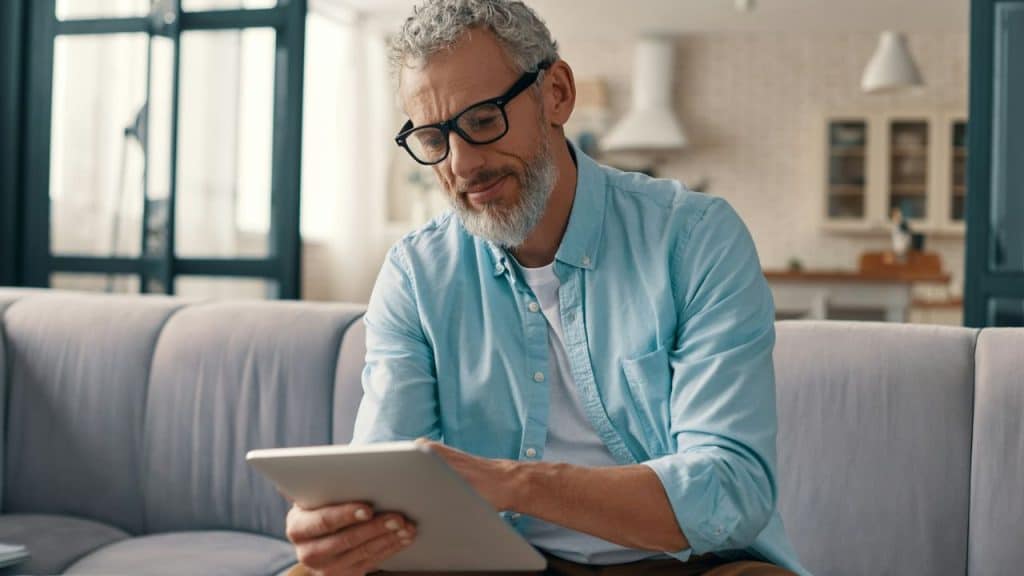Middle-aged man in a blue shirt and glasses sitting and using a tablet.