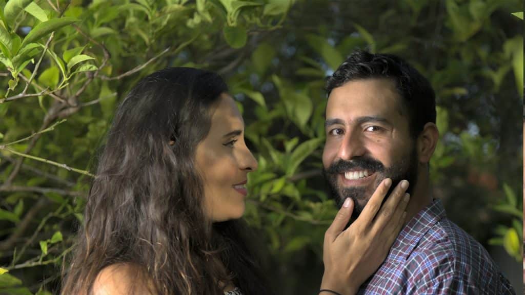 A woman with her hair open touching her boyfriend’s face and staring at him while standing next to him.