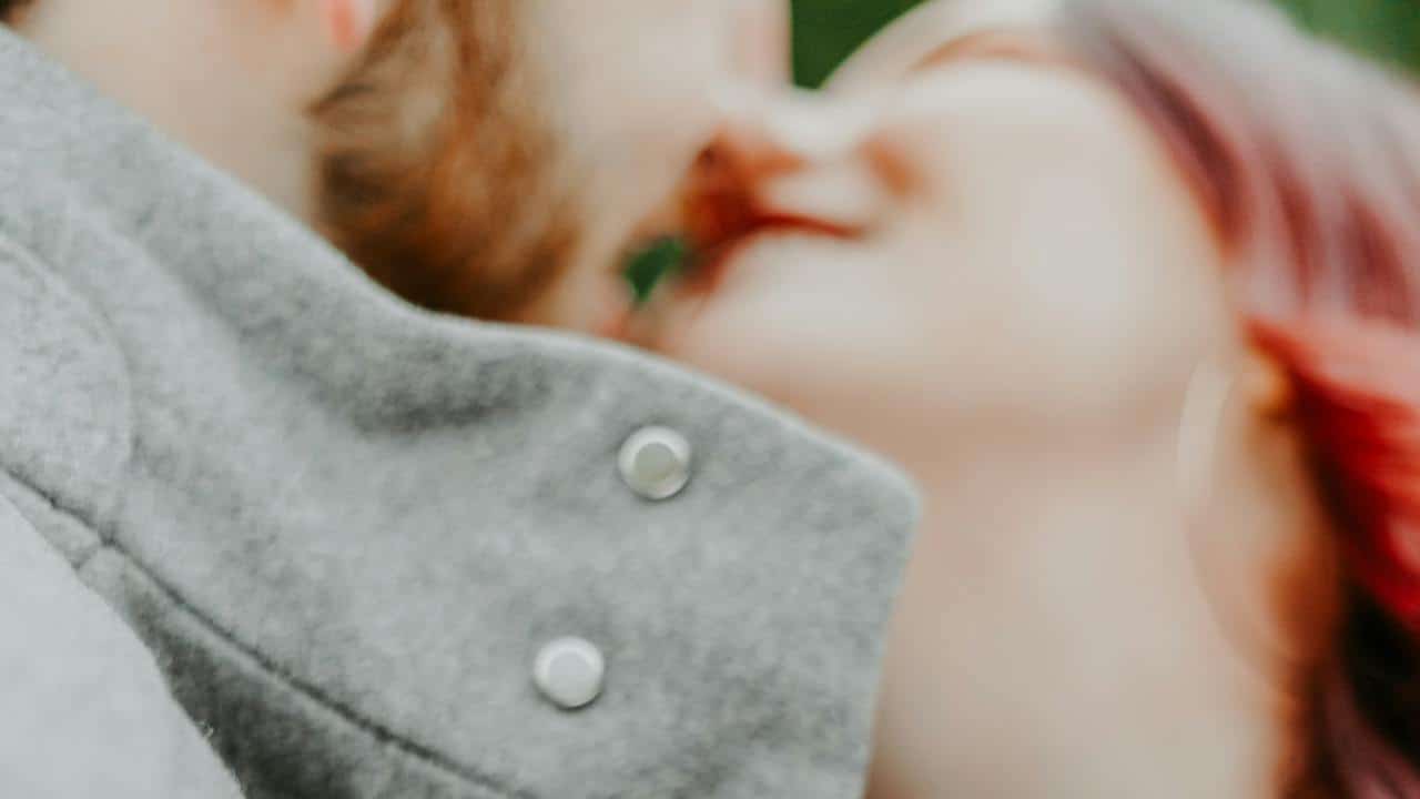 A blurry close-up of a couple kissing, focusing on the collar of a gray jacket.
