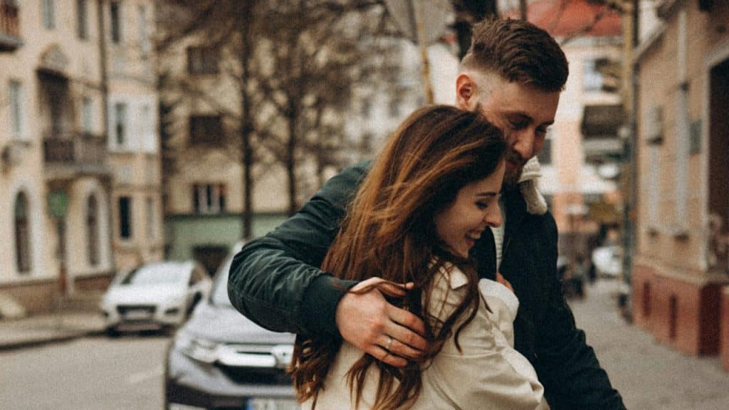 A man holding a smiling woman close as they stand on the street.