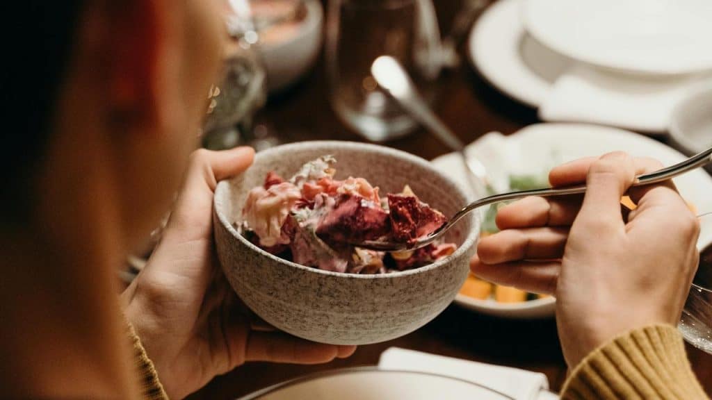 A person holding a bowl of mixed salad while eating with a spoon.