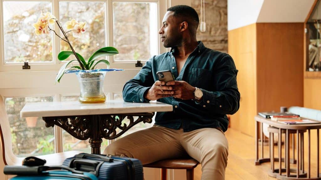 A person sitting indoors by a window holding a smartphone and looking outside.