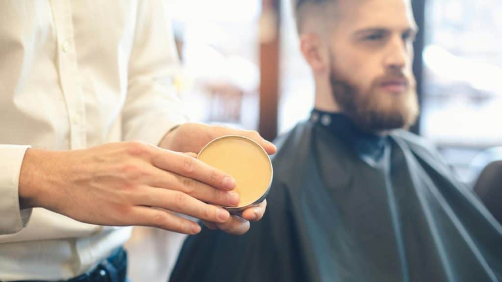 A barber holding a tin of hair product near a seated client.