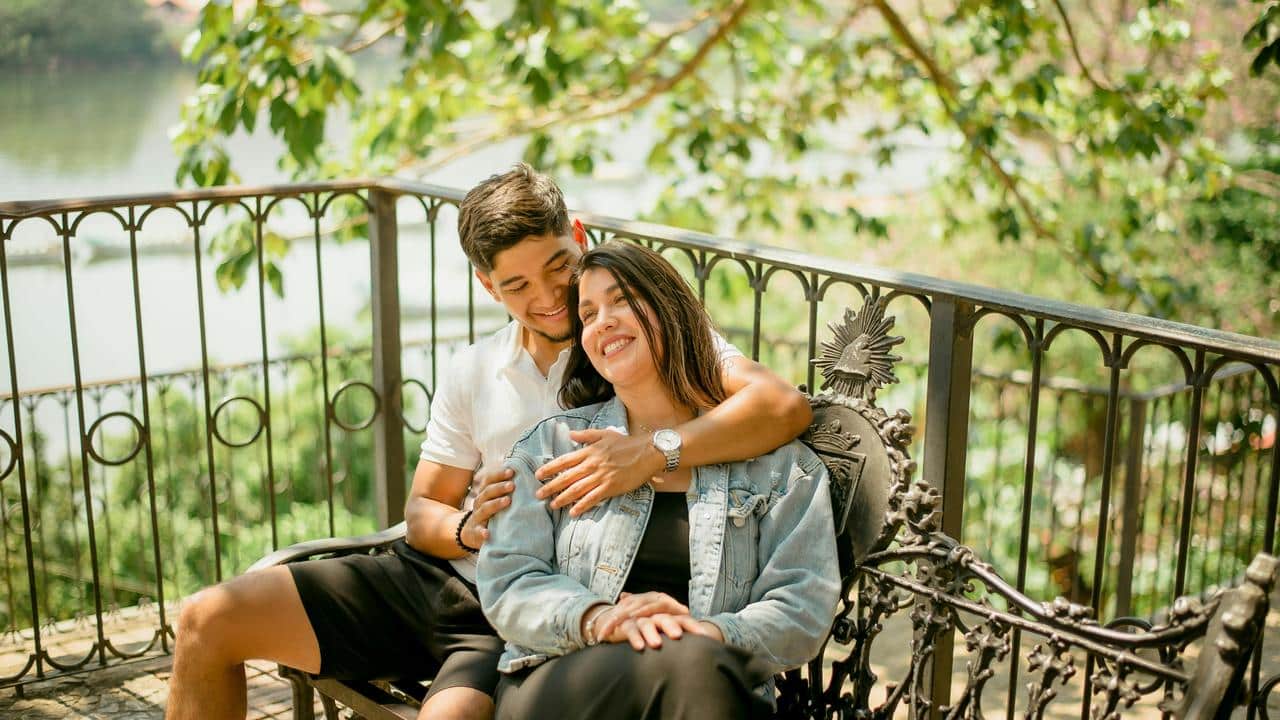 A couple sitting on an outdoor bench, smiling and embracing.