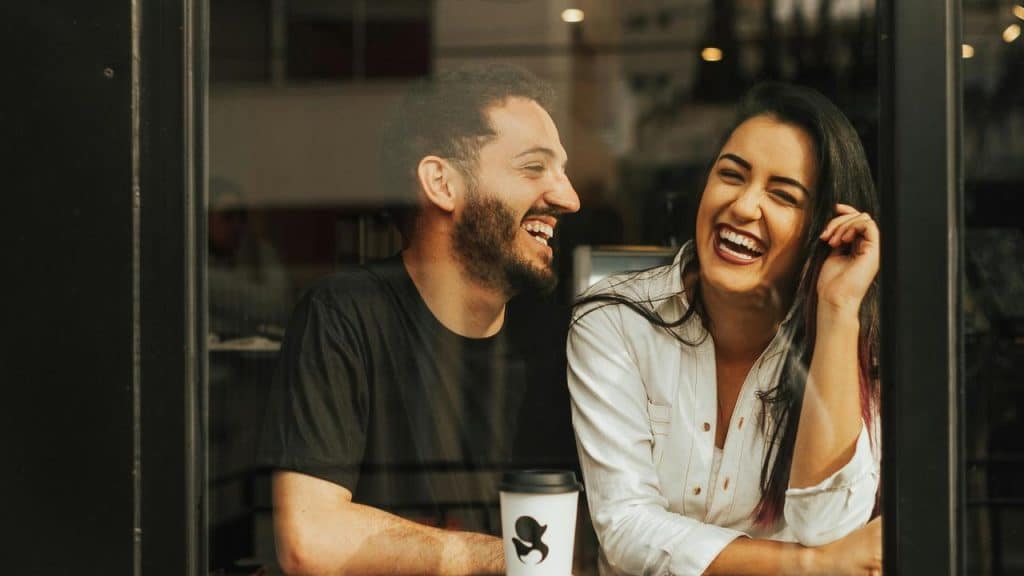 A man and woman laughing together at a café table.