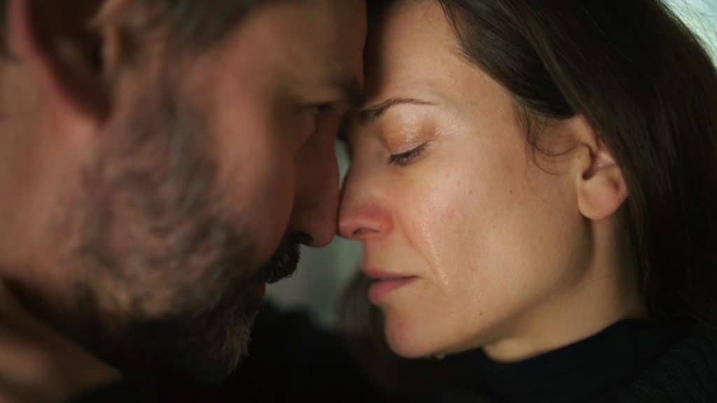 A close-up of a man and woman touching foreheads; the woman is crying.