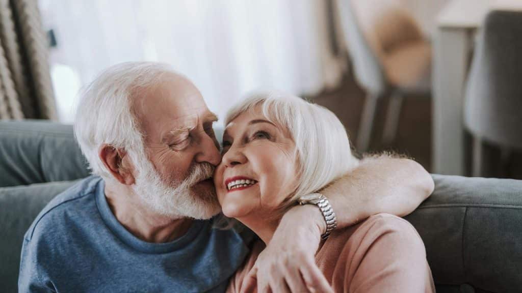 An older man kissing a smiling woman on the cheek while sitting together.