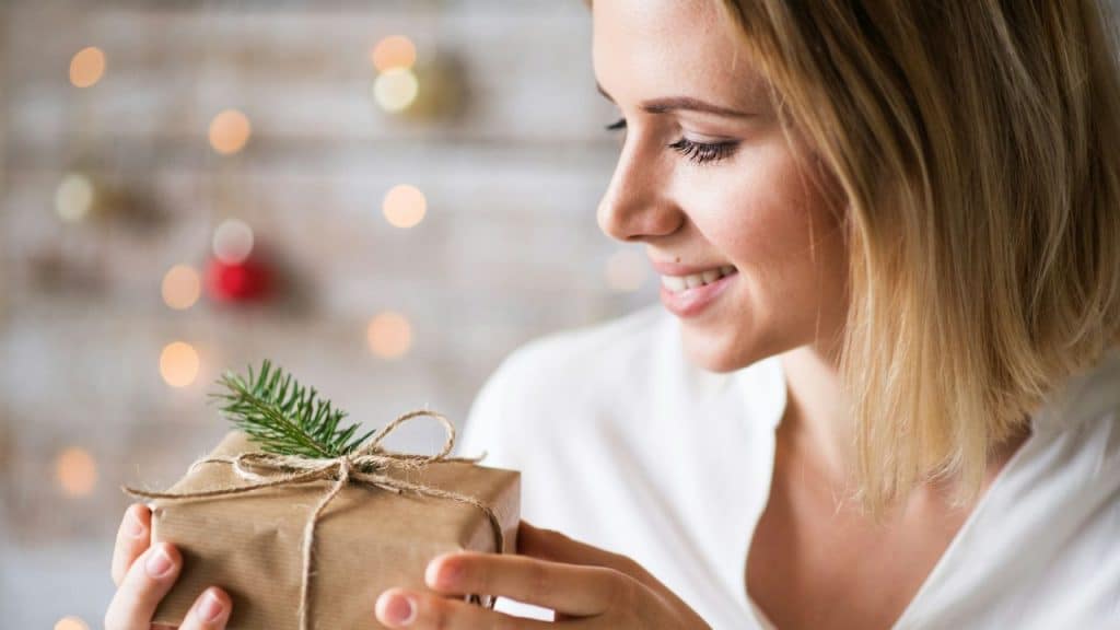 A smiling woman holds and looks down at a small wrapped gift box.