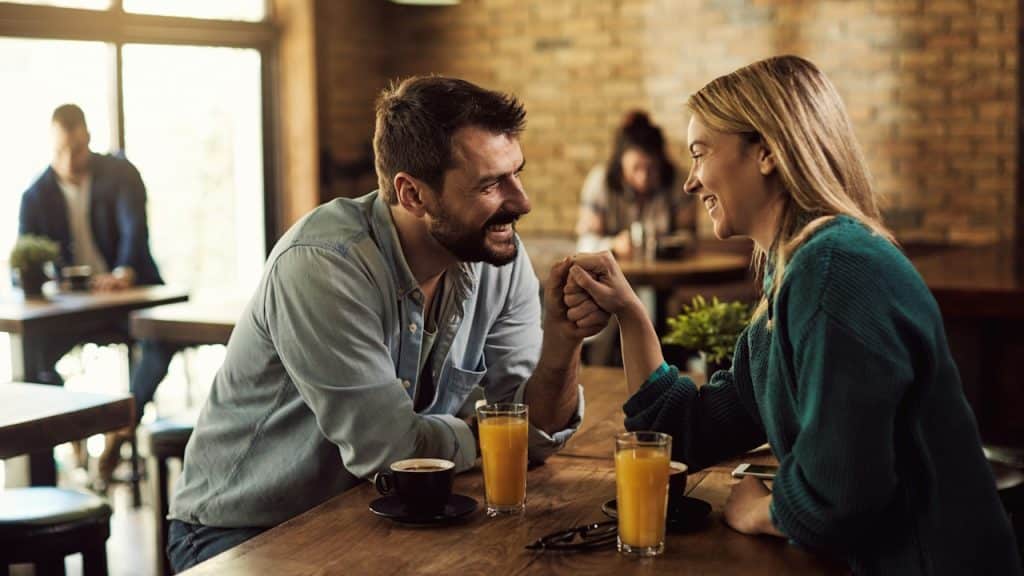 A happy couple communicating and holding hands while being on a date in a cafe.