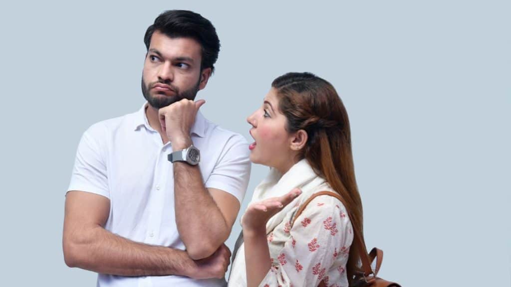 A man looks away while a woman speaks animatedly with an open hand gesture.
