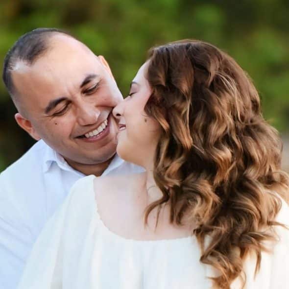 Couple embracing in a field of tall grass, smiling at each other.