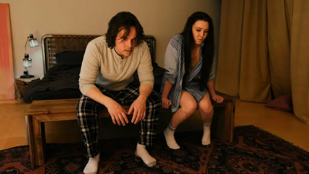 A couple sitting on a bench in their living room and looking bitter.
