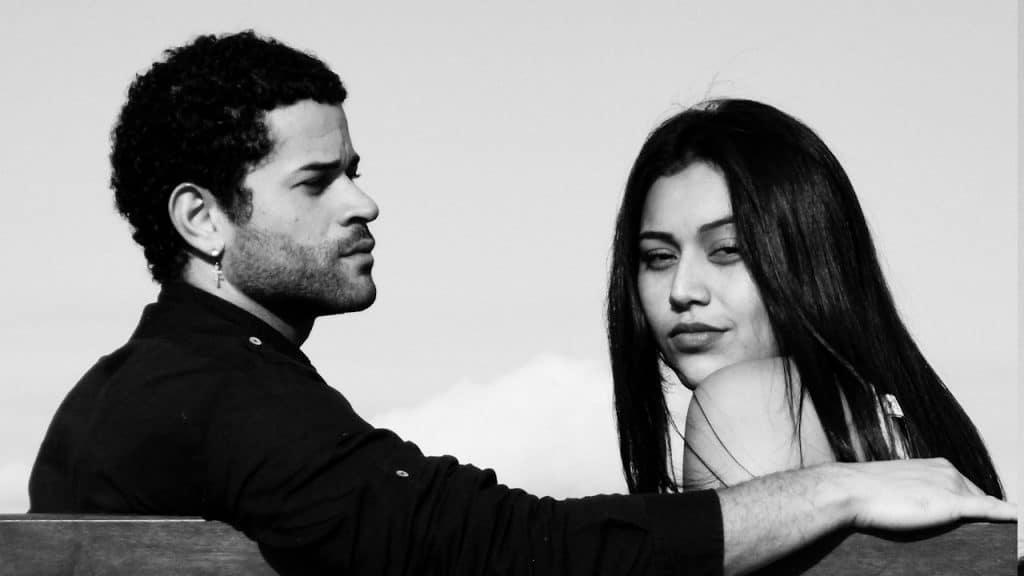A man and a woman sitting together on a wooden bench.