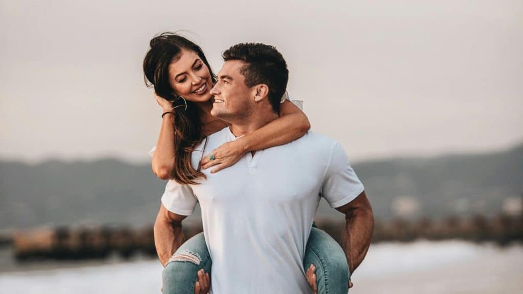 A smiling couple enjoying a piggyback ride on the beach.
