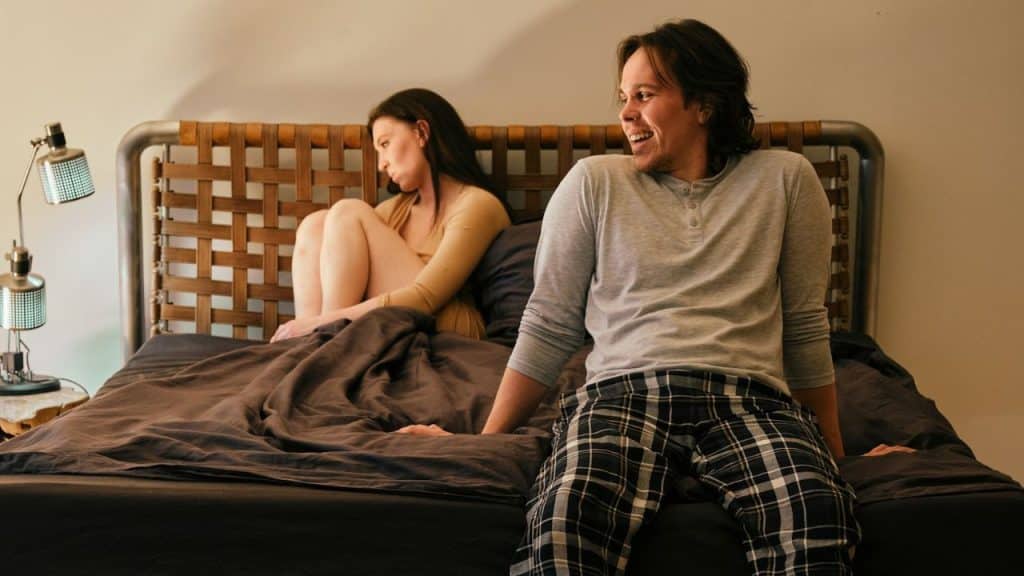 A man laughs and looks away from a woman sitting curled up on a bed.