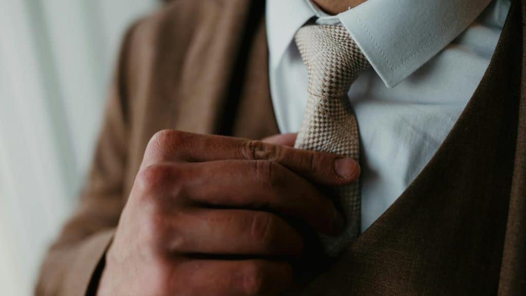A close-up of a person adjusting a tie while wearing a suit.