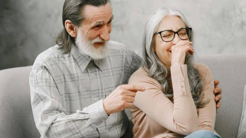 A senior couple sitting on a couch, laughing together.