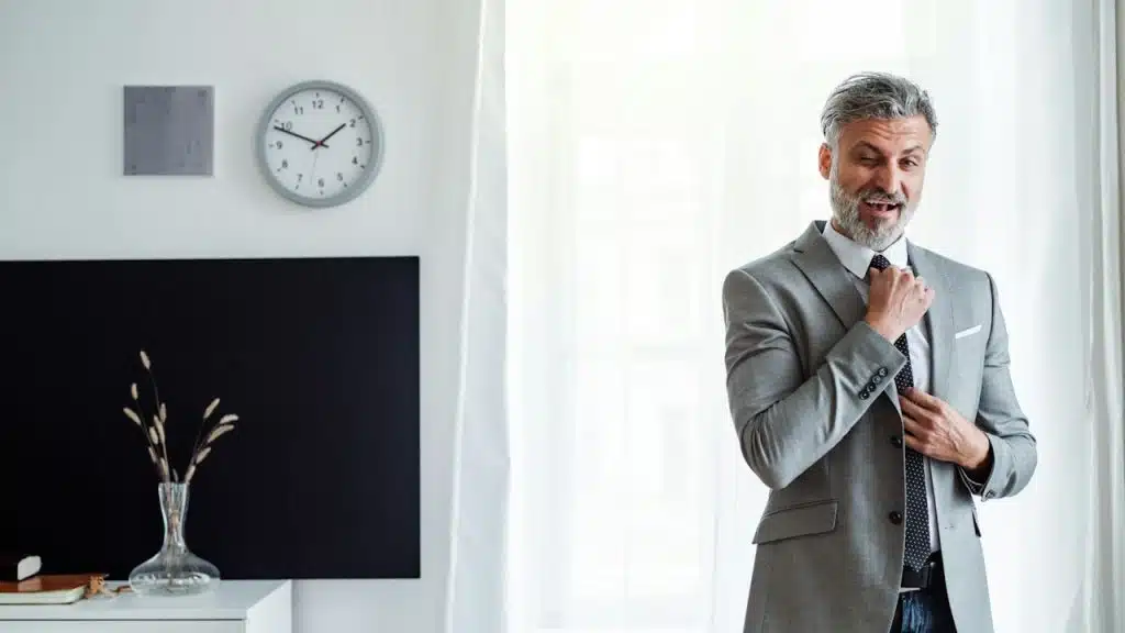 A bearded man wearing a suit and adjusting his tie.