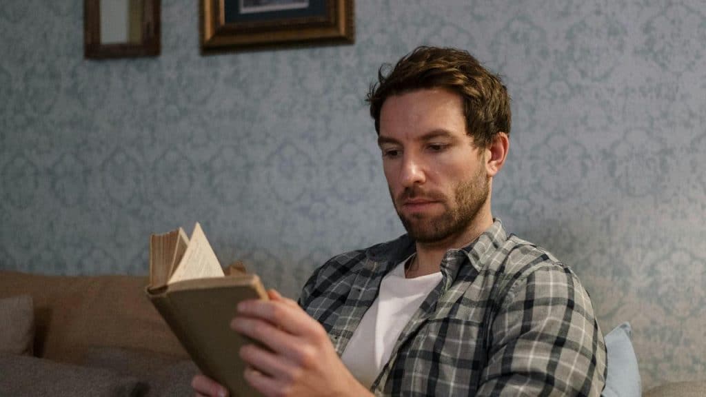 A man sitting on a couch reads a book.