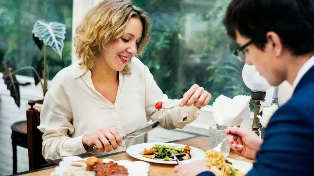 A woman in a white blouse smiles while eating dinner with a man in glasses.