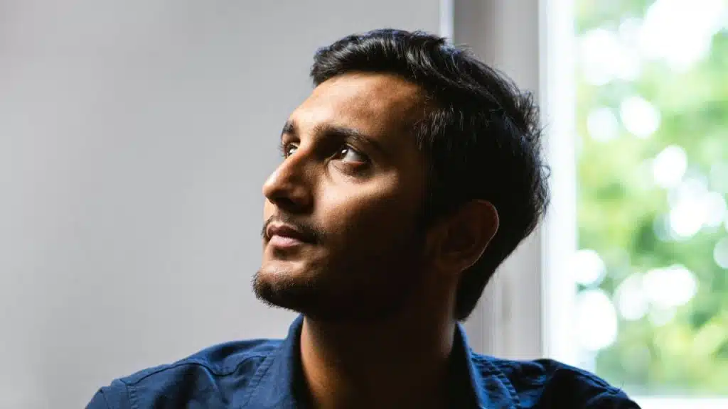 A man in a dark blue shirt looks upward and to the side toward a window.